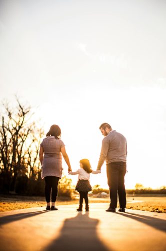 A family of three walks hand in hand at sunset, enjoying togetherness and warmth.